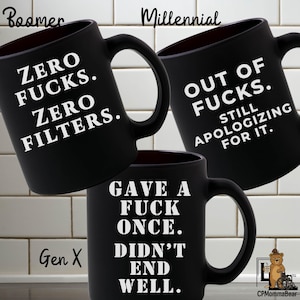 Puede incluir: Tres tazas de cerámica negras con texto blanco. Las tazas están etiquetadas como "Boomer", "Millennial" y "Gen X". La taza Boomer dice "ZERO FUCKS. ZERO FILTERS." La taza Millennial dice "OUT OF FUCKS. STILL APOLOGIZING FOR IT." La taza Gen X dice "GAVE A FUCK ONCE. DIDN'T END WELL."