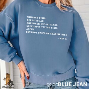 May include: A blue jean-colored sweatshirt with white text. The text includes a list of words and phrases, followed by "- GEN X". The bottom right corner of the sweatshirt reads "color: BLUE JEAN".