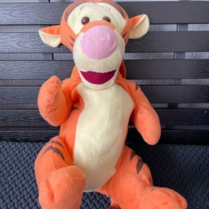 Op de afbeelding: Oranje en gele pluche speelgoed van Tigger uit Winnie de Poeh. Het speelgoed heeft een bruine neus en bruine voeten.