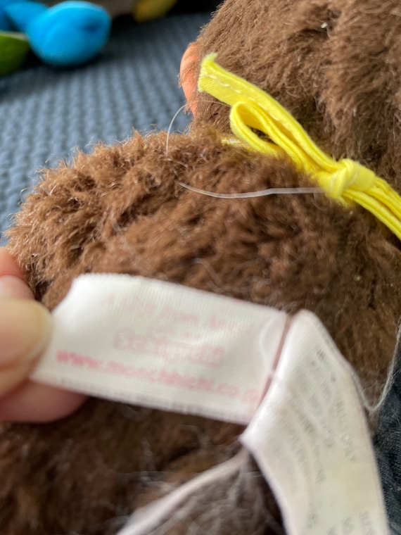 茶色のかわいいモンチッチのまばたき目が親指を吸っているぬいぐるみ