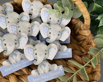 May include: A basket filled with blue and gray elephant baby shower favors. Each favor has a blue tag with the text "Ana's Baby Shower June 3rd, 2023".