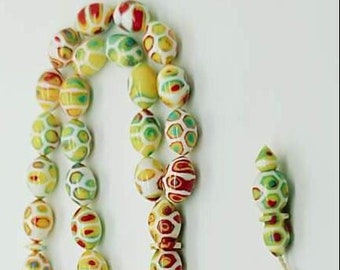 May include: A prayer bead strand featuring oval-shaped beads with a multi-colored marbled pattern in shades of yellow, green, red, and white. The strand includes a longer, tapered central bead and a small circular metal charm on the cord.