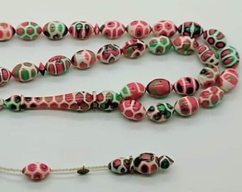May include: A prayer bead strand featuring oval-shaped beads with a marbled pattern in shades of pink, green, white, and black. The strand includes a central elongated focal bead and a dangling tassel section with smaller beads on a white cord.