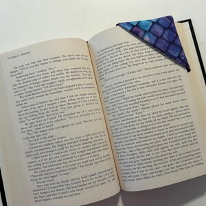 May include: An open book with a blue and purple fabric bookmark with a scale pattern. The book is open to a page with text about a character named Kieran.