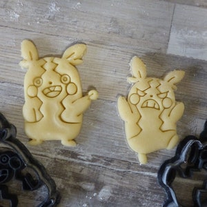 Könnte beinhalten: Zwei gelbe Ausstecher in Form eines Pokemon-Charakters mit unterschiedlichen Gesichtsausdrücken. Ein Ausstecher hat einen fröhlichen Ausdruck und der andere einen wütenden Ausdruck. Im Hintergrund befinden sich zwei schwarze Ausstecher.