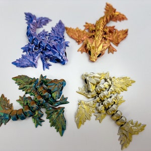 Könnte beinhalten: Vier kleine, detailreiche Drachenfiguren. Jeder Drache ist aus einem anderen Metall gefertigt und hat eine andere Farbe: blau, gold, grün und kupfer.