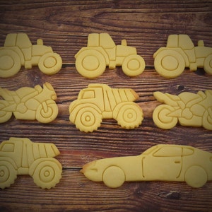 Könnte beinhalten: Ein Set aus neun gelben Zuckerkeksen in Form verschiedener Fahrzeuge, darunter ein Traktor, ein Kipplaster, ein Motorrad und ein Auto. Die Kekse sind auf einer Holzoberfläche angeordnet.