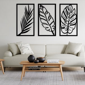 May include: Three black metal wall art pieces with leaf designs in rectangular frames. The artwork is displayed above a light-colored sofa and wooden coffee table, creating a modern, minimalist aesthetic. The room is decorated with neutral tones.