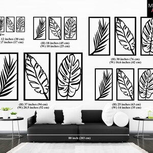 May include: Black metal wall art featuring stylized leaf designs in rectangular frames. The image shows various sizes, including a set of three 12-inch (30 cm) high panels and a large 37-inch (94 cm) high panel. The art is displayed above a black sofa.