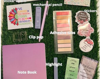 May include: A collection of stationery items including a canvas pencil case, notebook, stickers, decorative paper, adhesive tabs, a mechanical pencil, a highlighter, and bookmarks. The items are arranged on a green surface.