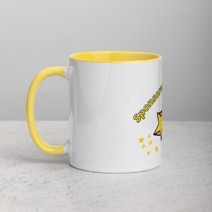 Puede incluir: Una taza de cer&aacute;mica blanca con un borde y un asa amarillos. La taza tiene una estrella amarilla y el texto "Sponsored by" impreso en ella.