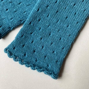 Pode incluir: Um par de aquecedores de braço de malha azul turquesa com uma borda festonada. Os aquecedores de braço têm um padrão de renda delicado.