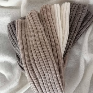 Puede incluir: Una bufanda suave y tejida en tonos marrones, beige y blanco. La bufanda está doblada por la mitad y tiene una textura acanalada.