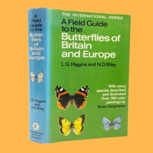 Puede incluir: Un libro verde titulado "A Field Guide to the Butterflies of Britain and Europe" de L.G. Higgins y N.D. Riley. La portada del libro presenta ilustraciones de mariposas de varios colores, incluyendo rojo, negro, amarillo y azul.