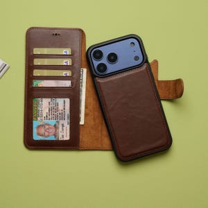May include: A brown leather wallet-style phone case with a black border, holding a phone with a blue camera module. The wallet has card slots, a driver's license, and cash. The driver's license is from Florida.