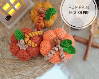 May include: Three crocheted pumpkins in orange and brown with green leaves. The pumpkins are on a woven brown surface. The text "PUMPKIN ENGLISH PDF" is in a white circle.