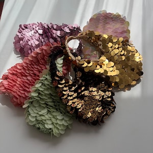 May include: A selection of sequined bags in shades of pink, gold, and green. The bags are round and covered in overlapping sequins. Some bags feature a leopard print design. The bags are a fashionable accessory.
