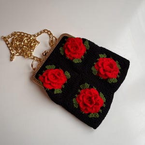 May include: A black crocheted purse with a gold chain strap and red rose embellishments.
