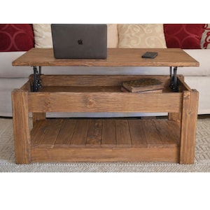 Op de afbeelding: Een rustieke, houten salontafel met een lift-top en een natuurlijke afwerking. De tafel heeft een onderste plank en een verborgen opbergvak. Een laptop en een smartphone liggen op het tafelblad. De tafel is ongeveer 122 cm lang, 61 cm breed en 46 cm hoog.