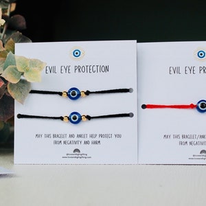 May include: Two cards with the text "Evil Eye Protection" and a blue evil eye charm bracelet on each card. The bracelet on the left card is black and the bracelet on the right card is red. The text on the cards reads "May this bracelet and anklet help protect you from negativity and harm."
