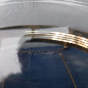 May include: A clear glass cake stand with a gold metal base. The base has three tiers and the glass top is etched with the word "Pessence".