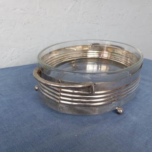 May include: A silver-plated glass serving dish with a decorative, geometric design. The dish has a clear glass bowl and a silver-plated base with a raised rim.