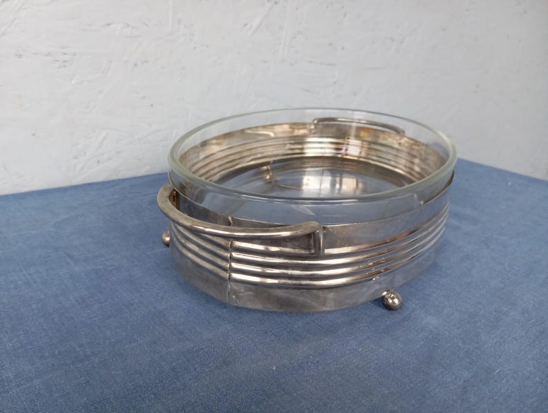 May include: A silver-plated glass serving dish with a decorative, geometric design. The dish has a clear glass bowl and a silver-plated base with a raised rim.