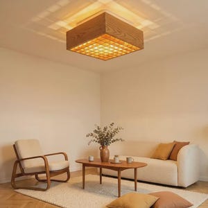 May include: A square ceiling light fixture featuring a light-toned wooden frame with a grid-patterned diffuser that casts a geometric light projection onto the ceiling. The fixture is mounted flush against the ceiling and emits a warm glow.