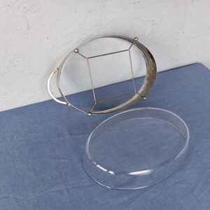 May include: A silver wire cake stand with a glass dome lid. The stand has a circular base and a wire frame that supports the dome.