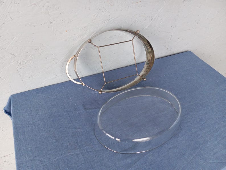 May include: A silver wire cake stand with a glass dome lid. The stand has a circular base and a wire frame that supports the dome.