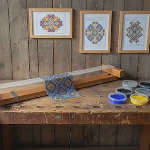 May include: A wooden bead loom with a partially completed geometric beaded tapestry featuring blue, yellow, and red patterns. Beside the loom are several small clear plastic containers filled with assorted colored glass beads.