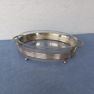 May include: Silver serving dish with a glass insert and three feet. The dish has two handles.