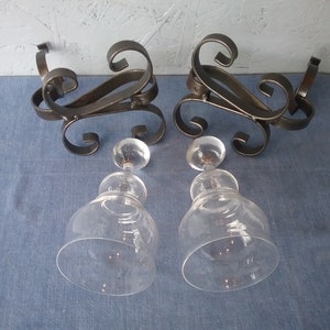 May include: Two clear glass decanters with ornate metal stands. The stands are black and have a scrolled design.