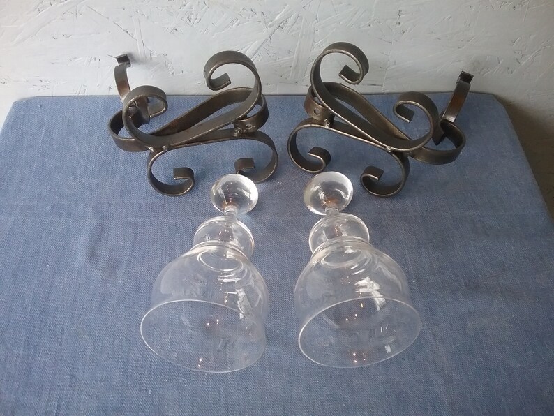 May include: Two clear glass decanters with ornate metal stands. The stands are black and have a scrolled design.