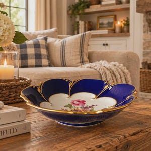 May include: A decorative porcelain bowl featuring a deep cobalt blue exterior and a scalloped rim with gold gilded edges. The interior is white with a central floral motif depicting a pink rose and small colorful blossoms on a smooth surface.