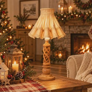 May include: A table lamp featuring a light-colored, pleated fabric lampshade with decorative trim and a carved wooden base with a twisted, spiral design. The lamp stands on a flat, circular base and emits a warm, soft glow from the light bulb.