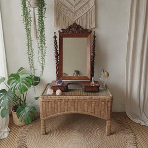 May include: A rectangular wooden vanity mirror with twisted side columns and a small base featuring two drawers, positioned on a rectangular wicker table with a glass top. The mirror frame is dark brown wood with carved decorative details.