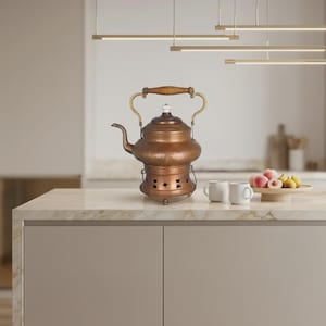 Peut inclure: Une bouilloire en cuivre avec une poignée en bois et un bouton blanc, reposant sur un support en cuivre assorti doté de découpes décoratives. La bouilloire présente un bec verseur incurvé et une finition métallique, près de deux tasses.