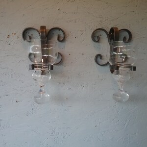 May include: Two black metal wall sconces with glass candle holders. The sconces have a decorative scroll design.