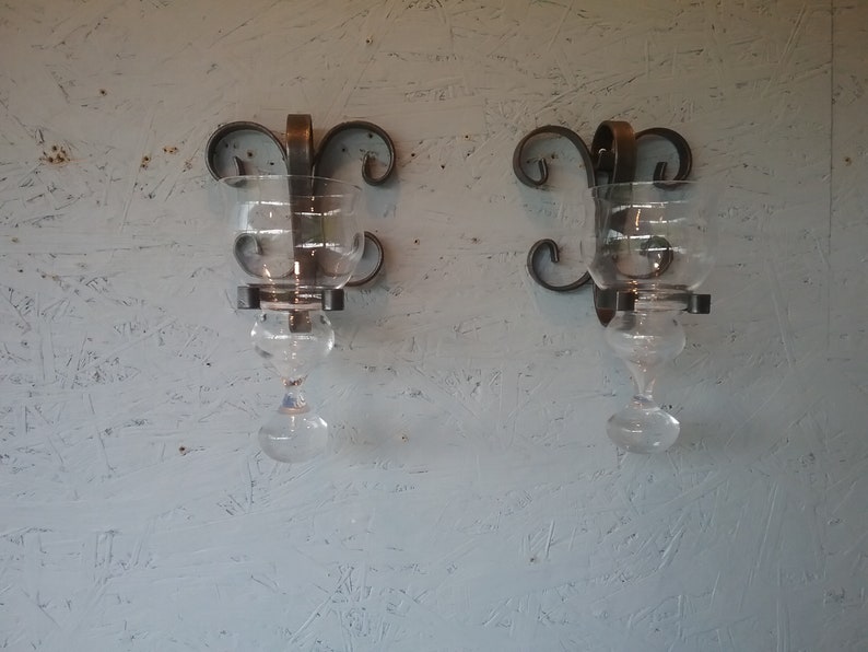 May include: Two black metal wall sconces with glass candle holders. The sconces have a decorative scroll design.
