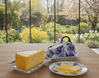 May include: A wedge of yellow cheese and sliced cheese on a white and blue floral patterned serving dish and plate. A matching cheese dome with a black handle sits nearby. The items are on a wooden table with a garden view.