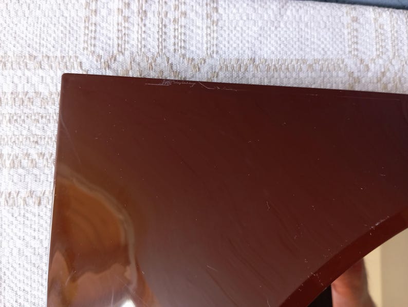 May include: A glossy, dark brown, triangular-shaped object with a smooth, reflective surface. The piece features a sharp, pointed corner and straight edges, showing subtle surface scratches and light reflections across its solid, dark-toned finish.