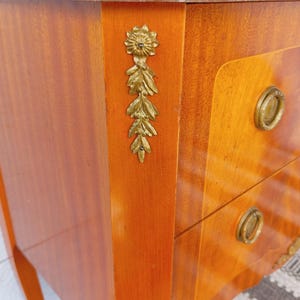 May include: A wooden nightstand with a marble top and brass hardware. The nightstand has two drawers and decorative brass floral accents. The wood has a warm, reddish-brown finish.