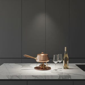 May include: A copper fondue pot with a long wooden handle sits on a matching circular metal stand with a burner underneath. Next to the pot are two clear glass wine glasses and a tall glass bottle filled with a light-colored liquid beverage.