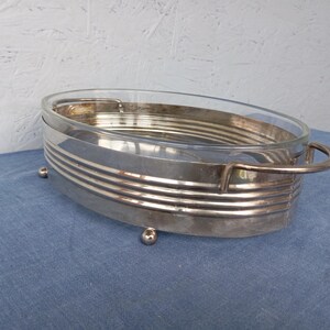May include: Silver serving dish with a glass insert and four small feet. The dish has a decorative, ribbed design around the edge.