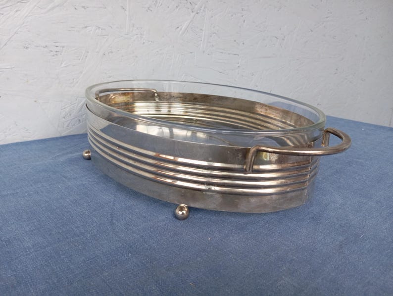 May include: Silver serving dish with a glass insert and four small feet. The dish has a decorative, ribbed design around the edge.