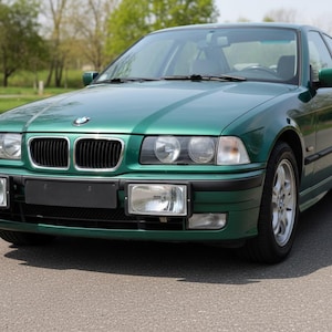 Puede incluir: Un sedán BMW verde con una parrilla negra y faros rectangulares. El coche está estacionado en una carretera pavimentada con una zona de césped y árboles en el fondo. El coche tiene ruedas plateadas.
