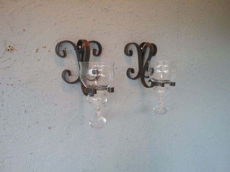 May include: Two black metal wall sconces with glass candle holders. The sconces have a decorative scroll design.