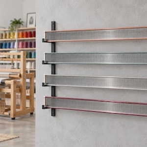Puede incluir: Un estante de pared con dos barras verticales de metal negro que sostienen cuatro repisas horizontales. Cada repisa sostiene un peine de tejer rectangular largo con una rejilla metálica y bordes de colores cobre, verde azulado, plata y rojo.