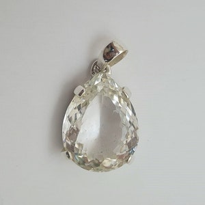 May include: A clear teardrop-shaped crystal pendant with a silver setting. The pendant is hanging from a silver bail.